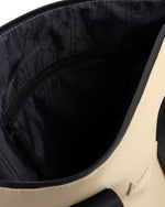 Close-up of the interior of a beige tote bag, showing a black zippered pocket lined with black patterned nylon and a small beige brand tag on the side.