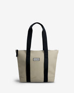 A Hunter tote bag in beige canvas with black webbed handles and vertical trim, featuring a small white 'Hunter' brand label on the front.