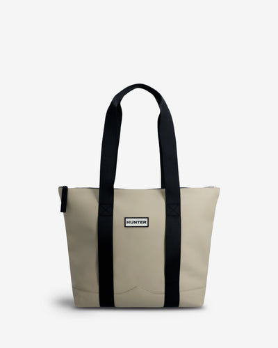 A Hunter tote bag in beige canvas with black webbed handles and vertical trim, featuring a small white 'Hunter' brand label on the front.