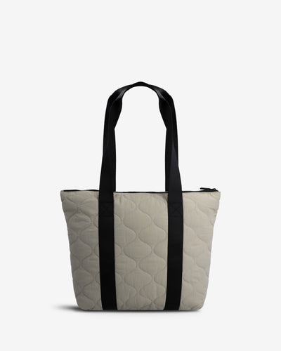 A light beige quilted tote bag with black shoulder straps, shown against a plain white background.