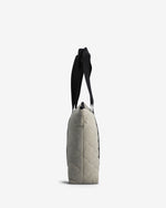 A side view of a quilted light beige shoulder bag with a black strap, shown against a plain white background.
