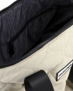 Close-up of a quilted off-white and black bag, showing the interior lining with a zigzag pattern, a black zipper pocket, and a black brand label reading HUNTER.