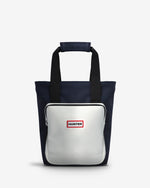 A Hunter tote bag featuring a navy blue body, black handles, and a large white front pocket with a red and white Hunter logo.