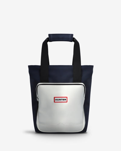 A Hunter tote bag featuring a navy blue body, black handles, and a large white front pocket with a red and white Hunter logo.