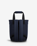 A navy blue tote bag with black shoulder straps, shown from the back against a light gray studio background.