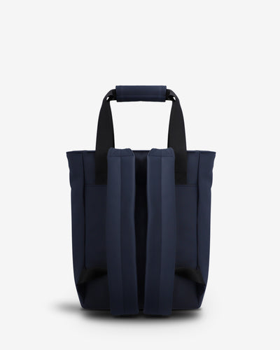 A navy blue tote bag with black shoulder straps, shown from the back against a light gray studio background.
