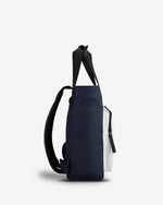 A navy blue tote bag with black shoulder straps and a white side pocket, shown from a side profile view against a light gray background.