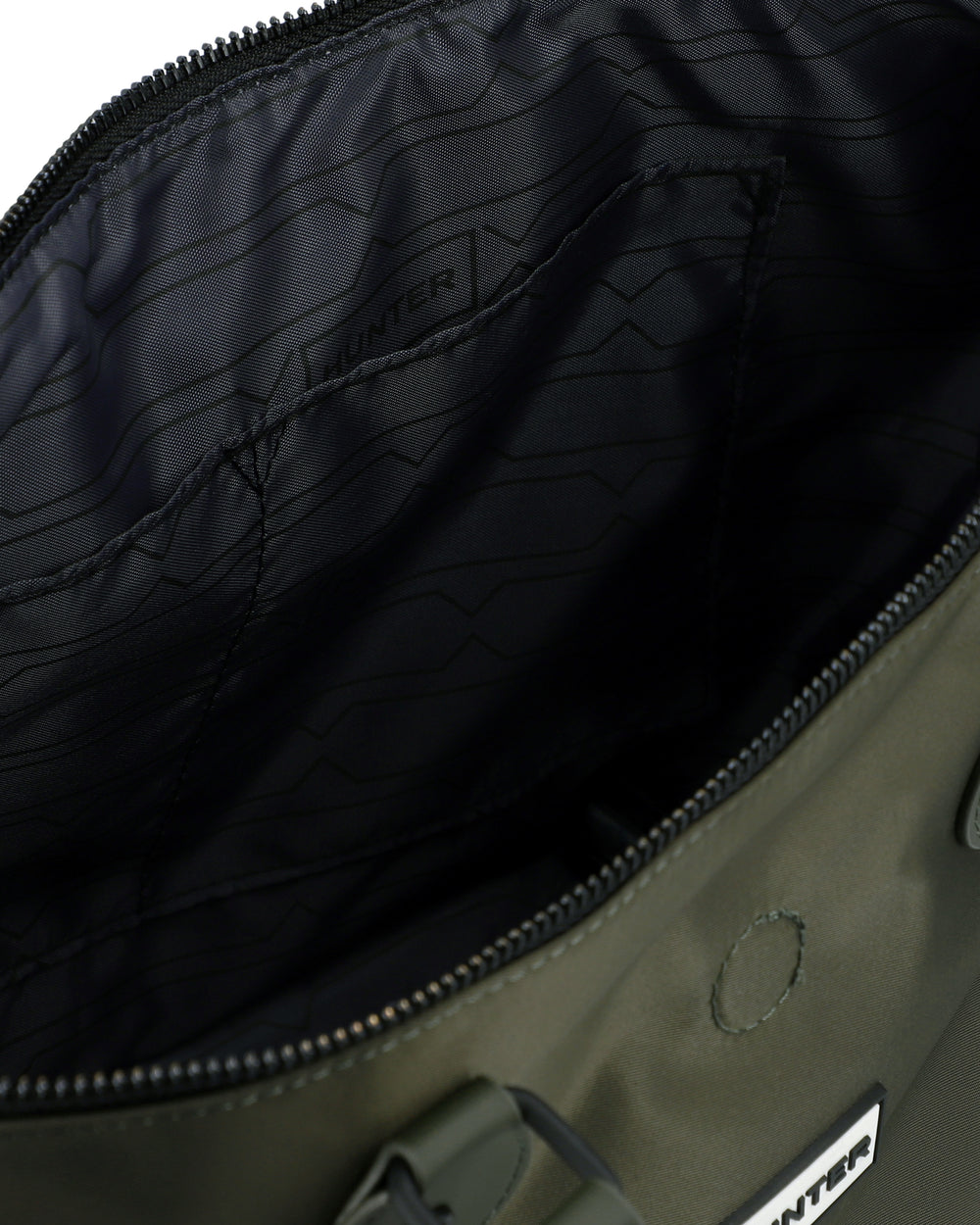 Close-up of the interior of an olive green bag, showing a black patterned lining with the brand name Hunter subtly printed inside, a black zipper, and part of the green exterior fabric with a metal rivet.