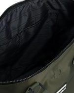 Close-up of the interior of an olive green bag, showing a black patterned lining with the brand name Hunter subtly printed inside, a black zipper, and part of the green exterior fabric with a metal rivet.