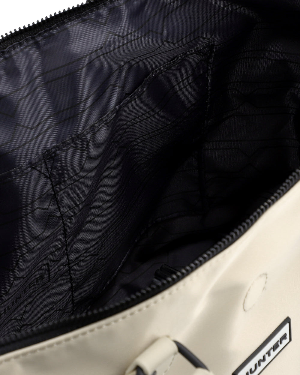 Close-up of the interior of a Hunter bag, showing a black zippered compartment with a black patterned lining and a cream-colored exterior.