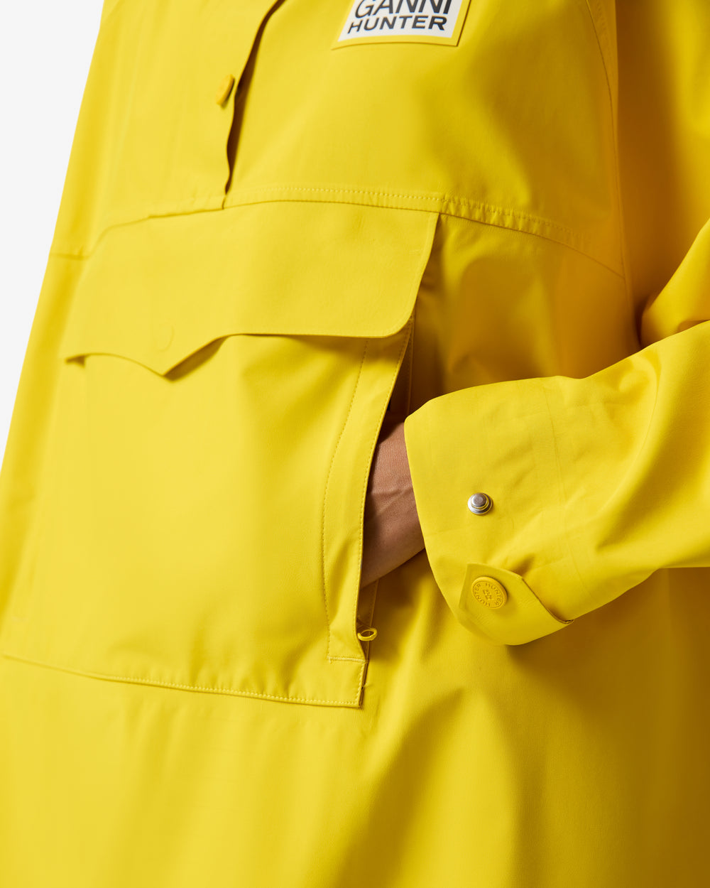 Displays a model wearing the Lemon 'Hunter' branded Unisex Ganni X Hunter Waterproof Poncho featuring the details on the pocket