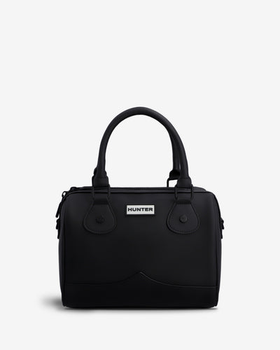 A black structured handbag with double top handles, a front flap pocket, and a small white Hunter brand plaque, photographed on a clean light gray background.