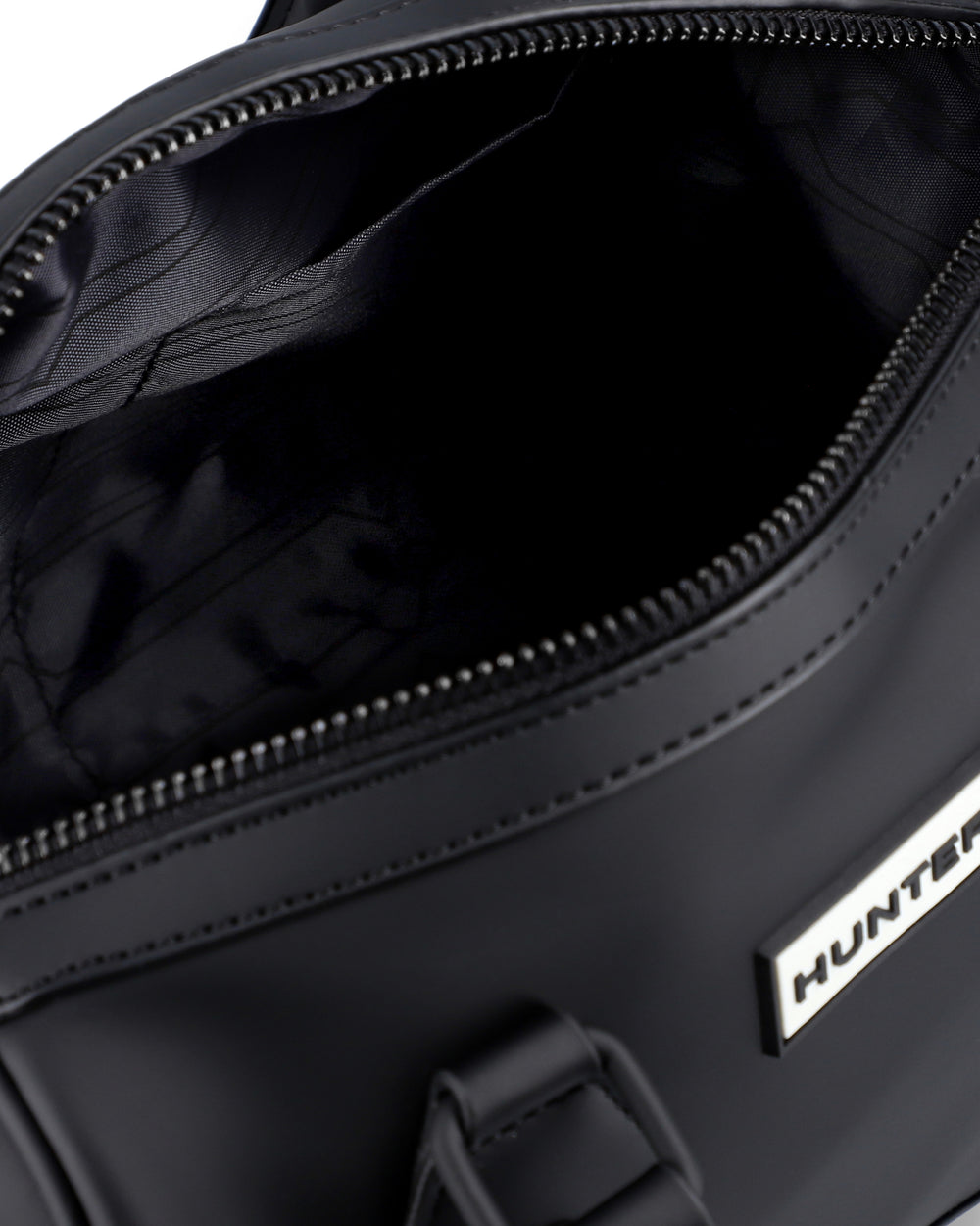 Close-up of a black duffel bag's open zipper compartment, showing the black interior lining and a silver metal brand plaque with the word HUNTER.