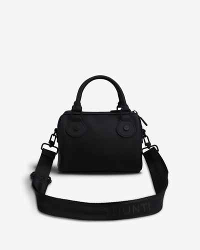 A black structured handbag with top handles and a wide matching shoulder strap, photographed on a clean light gray background. The strap has the brand name HUNTER printed in black on it.