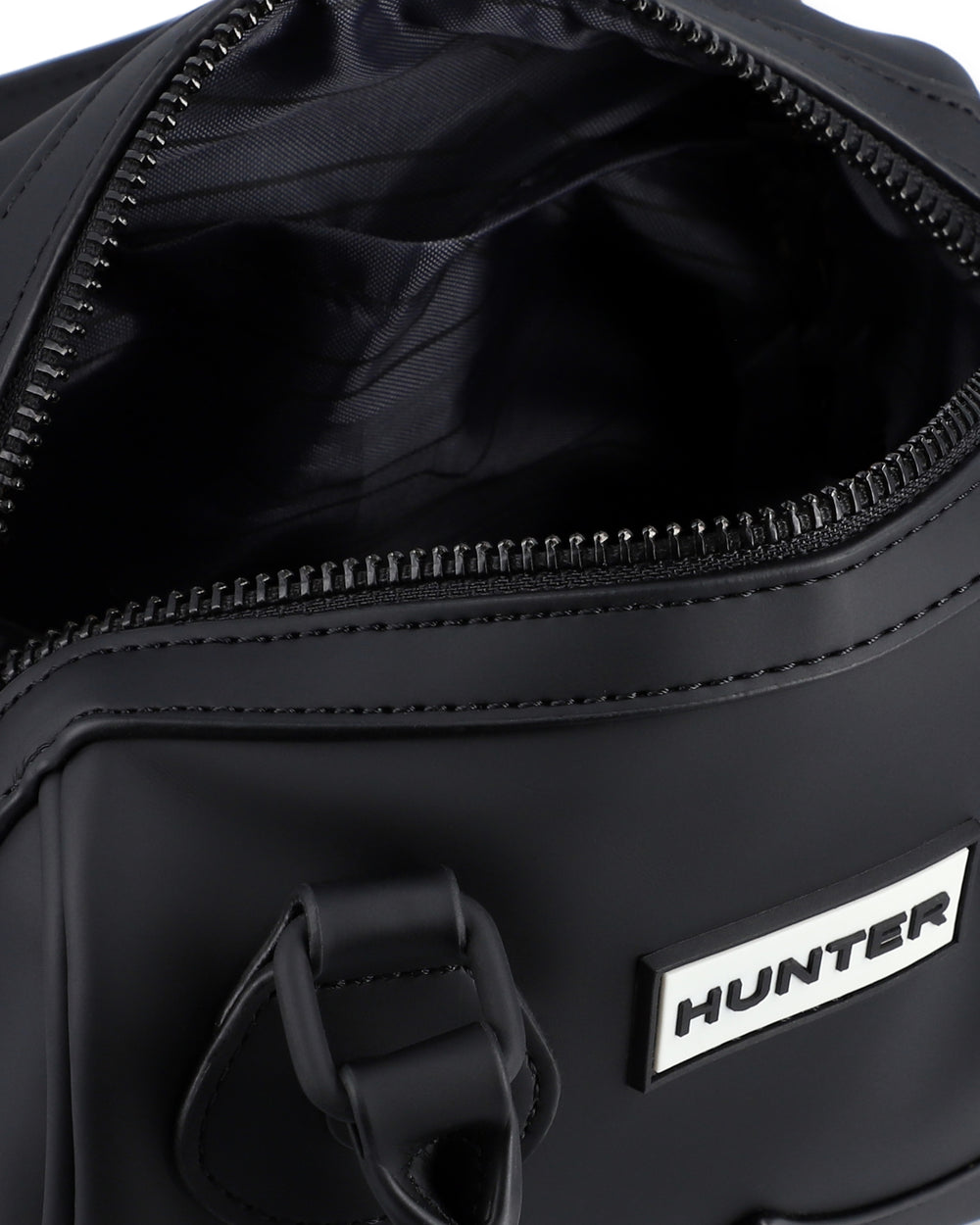 Close-up of a black duffel bag showing the open zipper opening, black interior lining, and a white rectangular patch with the brand name HUNTER.