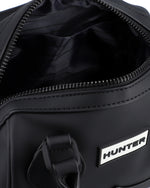 Close-up of a black duffel bag showing the open zipper opening, black interior lining, and a white rectangular patch with the brand name HUNTER.