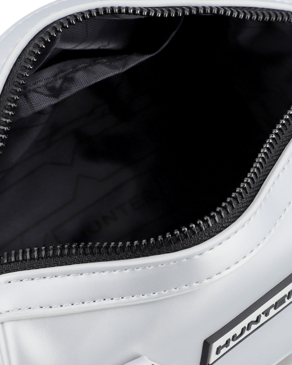 Close-up of a white bag's open zipper compartment, showing a black interior lining with subtle branding and black zipper trim.