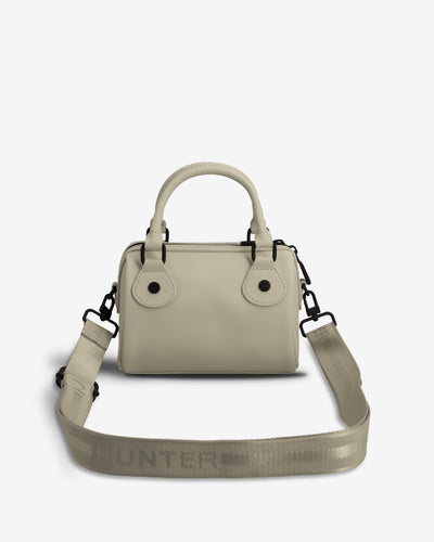 A light beige leather handbag with a top handle, double button closure, and an adjustable woven shoulder strap featuring the HUNTER logo, shown against a plain white background.