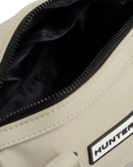 Close-up of a beige bag opening, showing a black interior lining and a black zipper. A white rectangular patch with the partial brand name HUNTER is visible on the side.