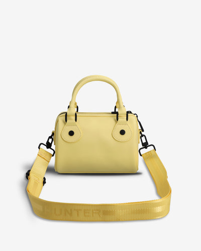 A light yellow structured handbag with a top handle, flap closure, and a matching wide shoulder strap laid flat in front. The strap has the brand name HUNTER printed across it.