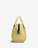 A small dome-shaped handbag in pale yellow faux leather with black strap details and gold-tone hardware, shown from the back against a light gray background.