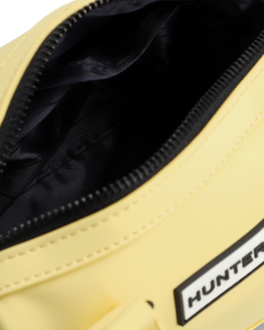 Close-up of a pale yellow bag with a black zipper opening, showing a black interior lining and a partial white brand patch reading HUNTER.